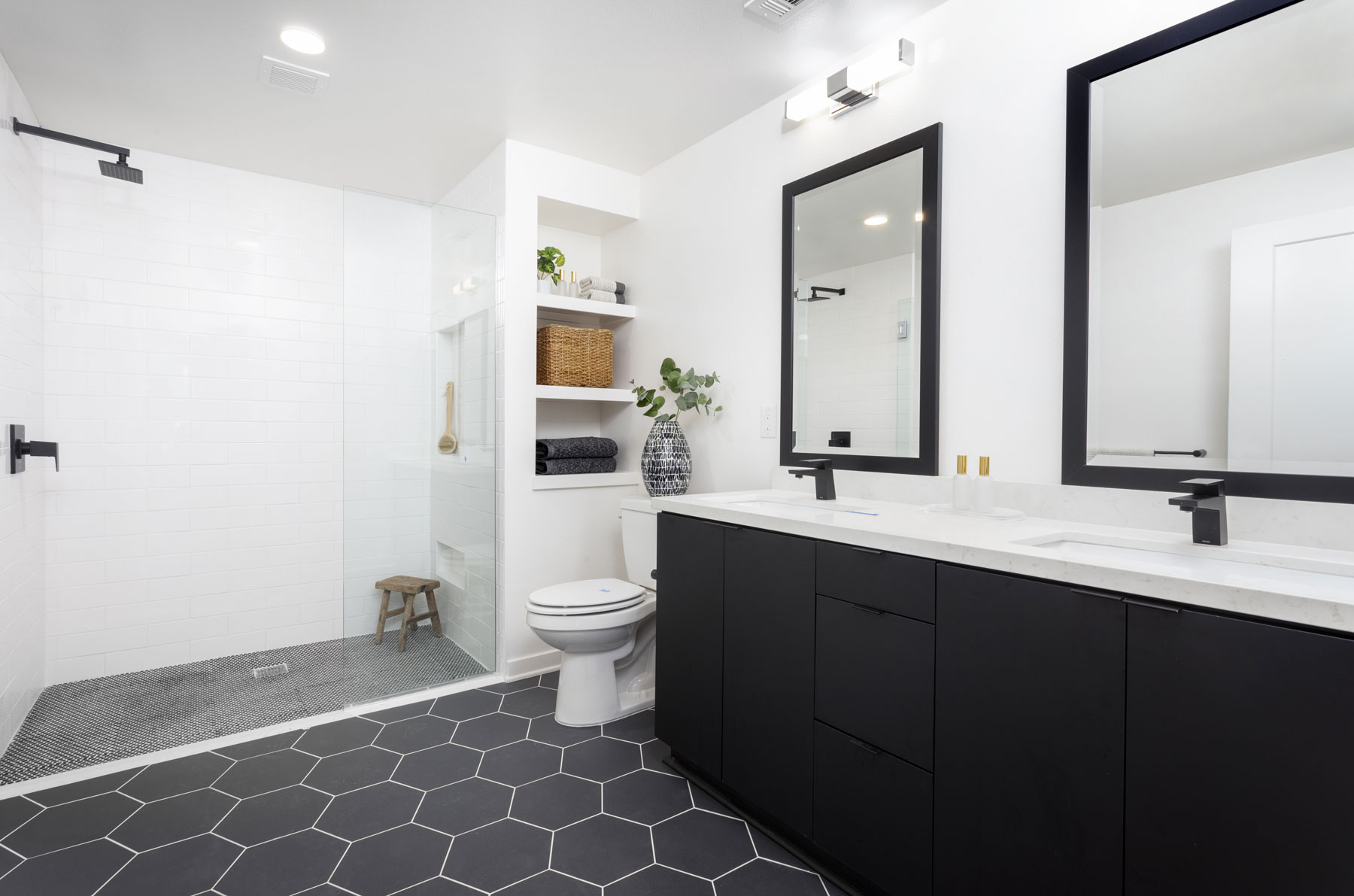 spacious modern bathroom with black cabinets, black hexagonal tiles, large glass walk in shower with rain shower head at Broadstone Archive
